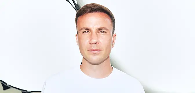 Fußballer Mario Götze im weißen T-Shirt schaut gerade in die Kamera, mit leicht zugekniffenen Augen (Foto)